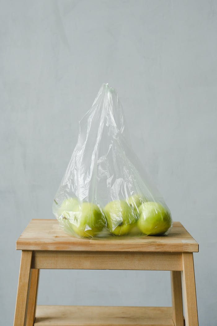 A minimalist photo of green apples in a plastic bag on a wooden stool, highlighting concepts of ecology and zero waste.